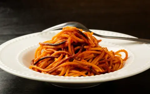 Spaghetti all'assassina, lekko przypalone, podane na białym talerzu z widelcem.