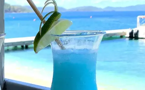 Niebieski drink z limonką, idealne proporcje Malibu z mlekiem, na tle błękitnego morza i plaży.