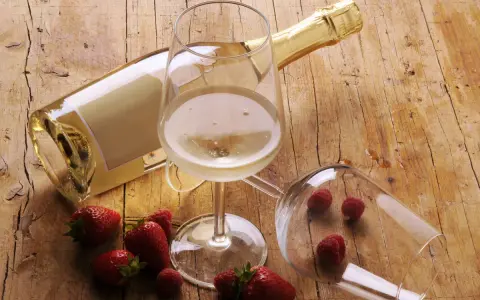 Butelka i kieliszki z winem musującym, obok truskawki i maliny. Idealne drinki z winem musującym na letnie popołudnie.