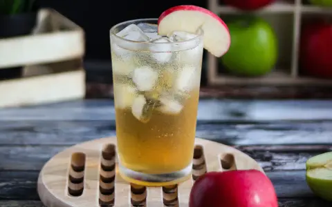 Orzeźwiający drink: whisky z sokiem jabłkowym, lodem i plasterkiem jabłka. Idealny na letnie popołudnie.