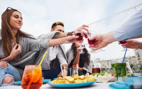 Grupa przyjaciół wznosi toast czerwonym aperitif drinkiem. Na stole owoce i inne przekąski.