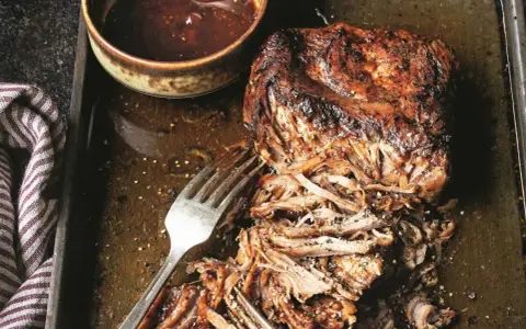 Soczyste pulled pork na blasze, gotowe do podania z sosem barbecue. Widoczne widelce ułatwiające rozrywanie mięsa.