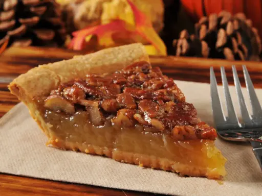 Kawałek pysznego, domowego pecan pie z orzechami i syropem, gotowy do zjedzenia.