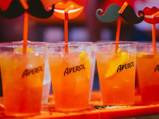 Idealne drinki na aperitif: orzeźwiające Aperole z lodem i plasterkiem pomarańczy, ozdobione zabawnymi wąsami i ustami.