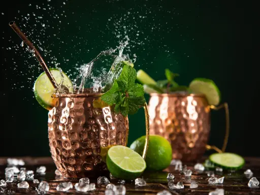 Orzeźwiający moscow mule drink z miętą i limonką, w miedzianych kubkach, z bryzgami wody i lodem.