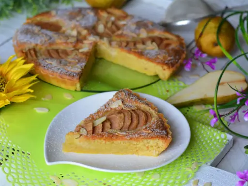 Pyszna tarta z gruszkami, posypana cukrem pudrem i płatkami migdałów, prezentuje się apetycznie na talerzyku. Obok cała tarta, gruszki i słonecznik.