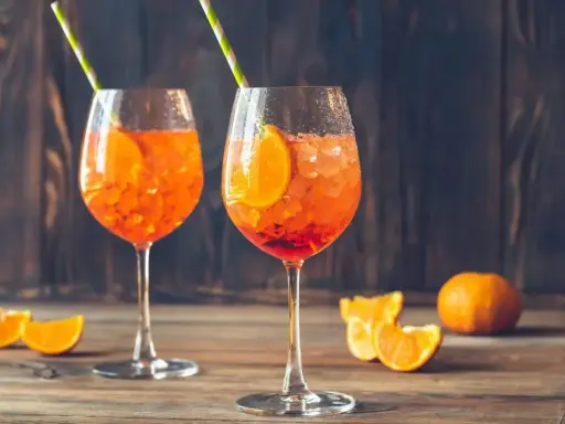 Dwa orzeźwiające aperol z prosecco, ozdobione plastrami pomarańczy i słomkami, na drewnianym blacie.