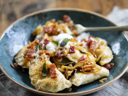 Pyszne pierogi z boczkiem i cebulką, polane śmietaną. Idealne, gdy zastanawiasz się, jak zrobić pierogi.