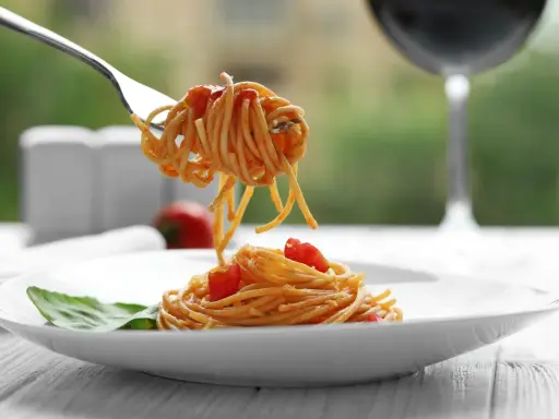 Idealne spaghetti z sosem pomidorowym na talerzu, a w tle kieliszek czerwonego wina. Zastanawiasz się, jakie wino do spaghetti wybrać?
