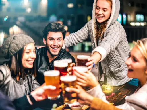 Grupa przyjaciół wznosi toasty piwem, śmiejąc się i ciesząc wieczorem. Czy piwo ma gluten? To pytanie może nurtować, ale dziś liczy się wspólna zabawa.