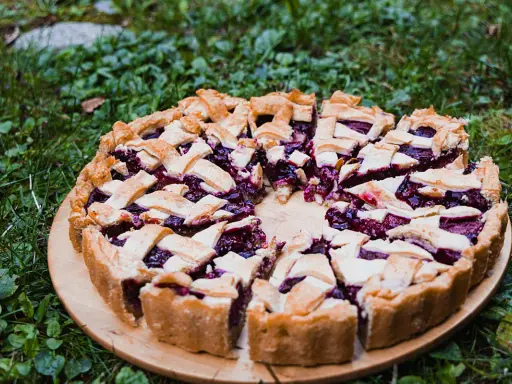 Pyszna tarta ze śliwkami, z kratką z ciasta, na drewnianej desce, wśród zielonej trawy.