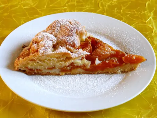 Pyszna tarta z morelami, posypana cukrem pudrem, na białym talerzu.