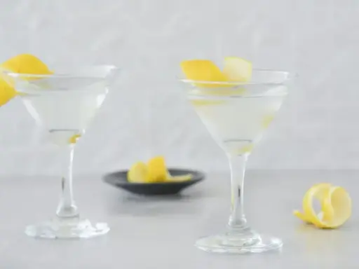 Dwa eleganckie kieliszki z orzeźwiającym martini, ozdobione skórką cytrynową. Idealne na letnie wieczory.