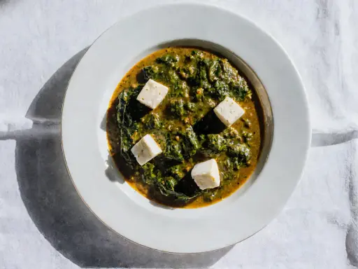 Palak paneer w białej misce, z kostkami sera paneer pływającymi w zielonym sosie ze szpinaku.