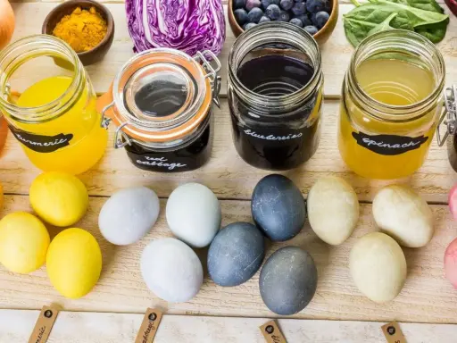 Słoiki z barwnikami z kurkumy, czerwonej kapusty, borówek i szpinaku do naturalnego farbowania jajek. Obok kolorowe jajka.