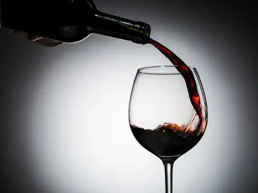 Czerwone wino leje się z butelki do kieliszka. Czy wino jest zdrowe? To pytanie towarzyszy tej chwili.
