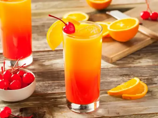 Dwa drinki tequila sunrise z pomarańczą i wiśnią, na drewnianym stole.