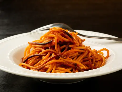 Spaghetti all'assassina, lekko przypalone, podane na białym talerzu z widelcem.