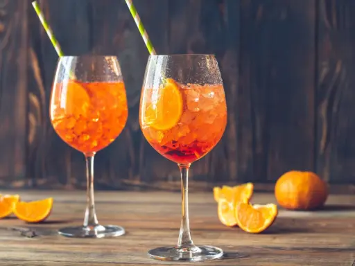 Dwa orzeźwiające drinki aperol ze sprite, udekorowane plasterkami pomarańczy i słomkami, na drewnianym tle.