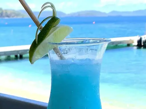 Niebieski drink z limonką, idealne proporcje Malibu z mlekiem, na tle błękitnego morza i plaży.