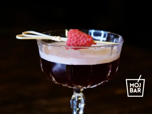 Elegancki koktajl Clover Club z maliną na patyczku, serwowany w kieliszku z logo MOJ BAR.