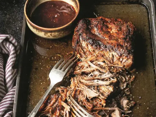 Soczyste pulled pork na blasze, gotowe do podania z sosem barbecue. Widoczne widelce ułatwiające rozrywanie mięsa.