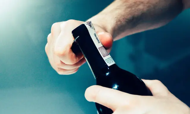 Dwie dłonie otwierają butelkę z winem domowym. Chcesz wiedzieć, jak zmierzyć zawartość alkoholu w winie domowym?