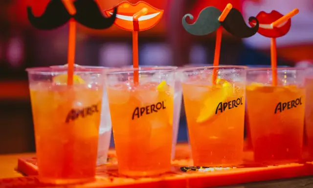 Idealne drinki na aperitif: orzeźwiające Aperole z lodem i plasterkiem pomarańczy, ozdobione zabawnymi wąsami i ustami.