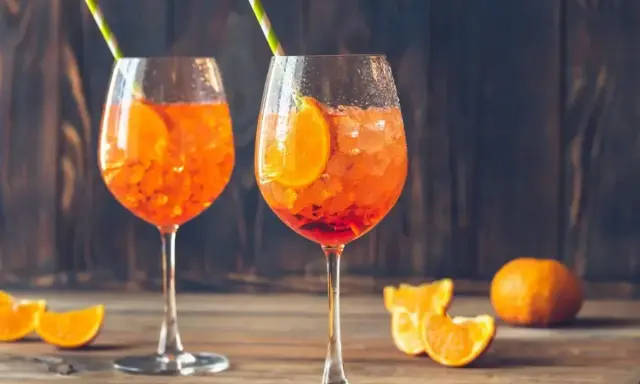 Dwa orzeźwiające aperol z prosecco, ozdobione plastrami pomarańczy i słomkami, na drewnianym blacie.