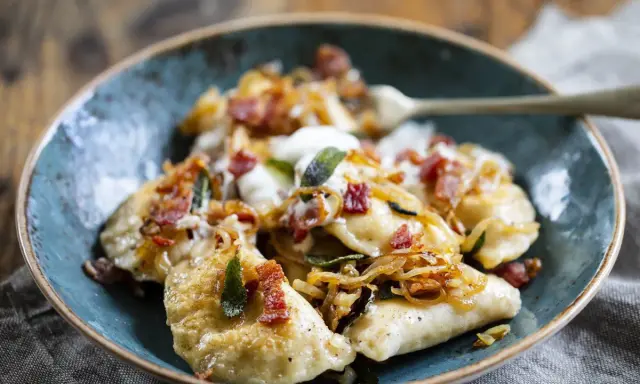 Pyszne pierogi z boczkiem i cebulką, polane śmietaną. Idealne, gdy zastanawiasz się, jak zrobić pierogi.