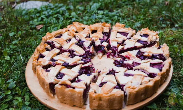 Pyszna tarta ze śliwkami, z kratką z ciasta, na drewnianej desce, wśród zielonej trawy.