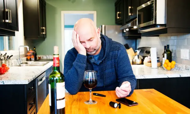 Zamyślony mężczyzna przy stole z winem i glukometrem. Czy czerwone wino obniża cukier?