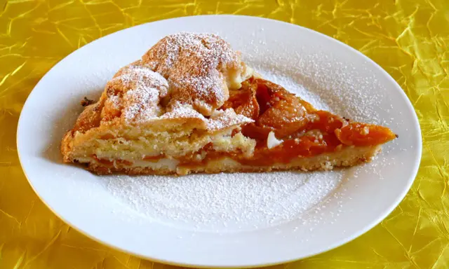 Pyszna tarta z morelami, posypana cukrem pudrem, na białym talerzu.