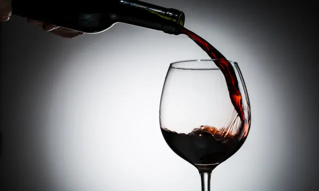 Czerwone wino leje się z butelki do kieliszka. Czy wino jest zdrowe? To pytanie towarzyszy tej chwili.