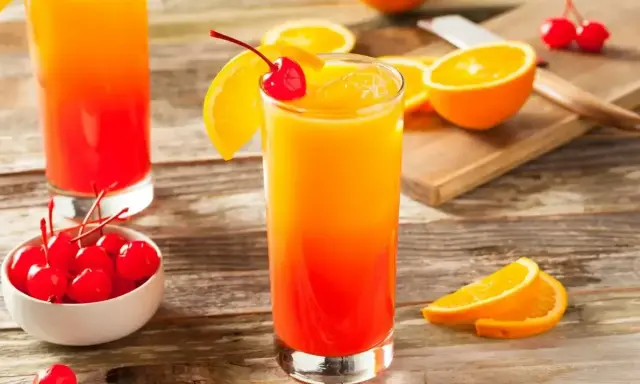 Dwa drinki tequila sunrise z pomarańczą i wiśnią, na drewnianym stole.