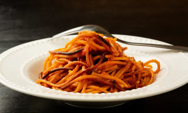 Spaghetti all'assassina, lekko przypalone, podane na białym talerzu z widelcem.