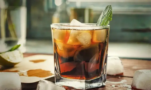 Orzeźwiający gin z colą, z lodem i miętą, na drewnianym blacie. Idealny na letnie wieczory.