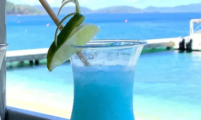 Niebieski drink z limonką, idealne proporcje Malibu z mlekiem, na tle błękitnego morza i plaży.