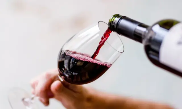 Czerwone wino nalewa się do kieliszka, tworząc idealną lampkę wina wieczorem.