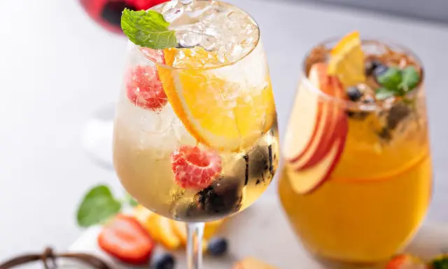 Orzeźwiający drink z prosecco, malinami, pomarańczą i miętą. Obok drugi napój z brzoskwinią i pomarańczą.