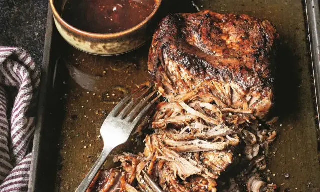 Soczyste pulled pork na blasze, gotowe do podania z sosem barbecue. Widoczne widelce ułatwiające rozrywanie mięsa.