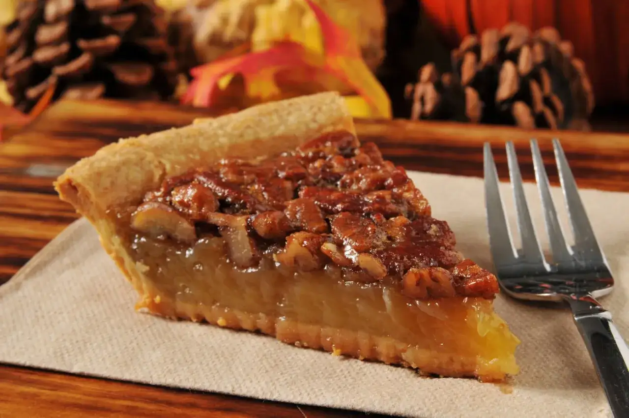 Kawałek pysznego, domowego pecan pie z orzechami i syropem, gotowy do zjedzenia z widelcem.