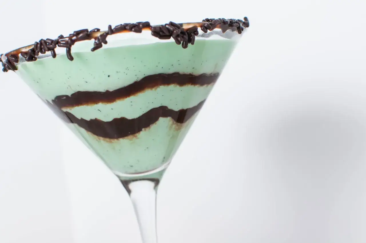 Zielony drink Grasshopper w kieliszku martini, ozdobiony czekoladowym sosem i posypką.