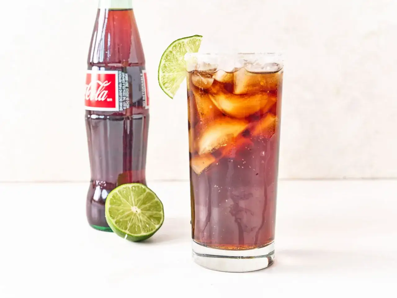 Orzeźwiająca tequila z colą, podana z lodem i limonką, obok butelki Coca-Coli. Idealna na upalne dni.