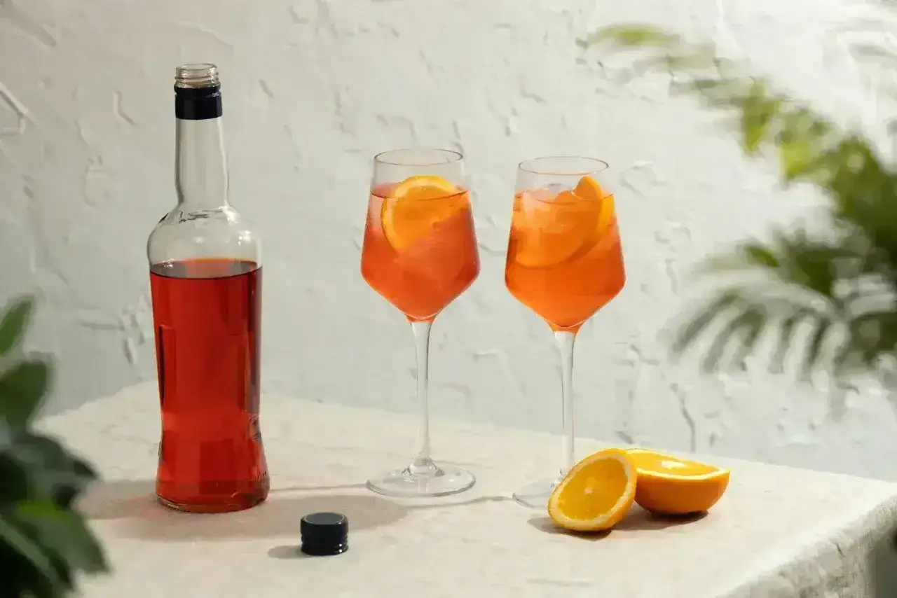 Dwa orzeźwiające drinki aperol z prosecco, ozdobione plasterkami pomarańczy, stoją obok butelki aperolu.