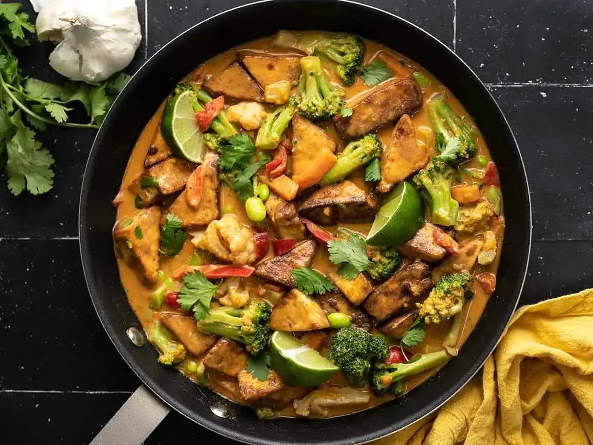 Aksamitne tofu w sosie orzechowym z brokułami, kalafiorem i edamame, udekorowane limonką i kolendrą.