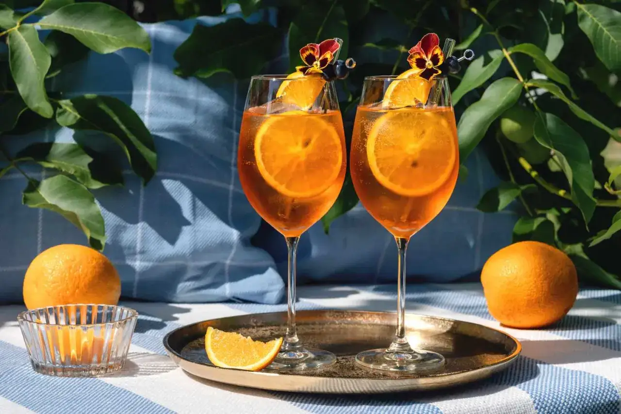 Dwa orzeźwiające aperol z tonikiem, udekorowane plasterkami pomarańczy i kwiatami, gotowe do degustacji w letni dzień.