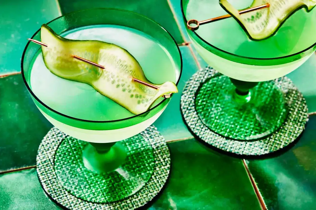 Orzeźwiający drink z martini, ozdobiony plasterkiem ogórka na wykałaczce, w zielonym kieliszku na błyszczącej podstawce.
