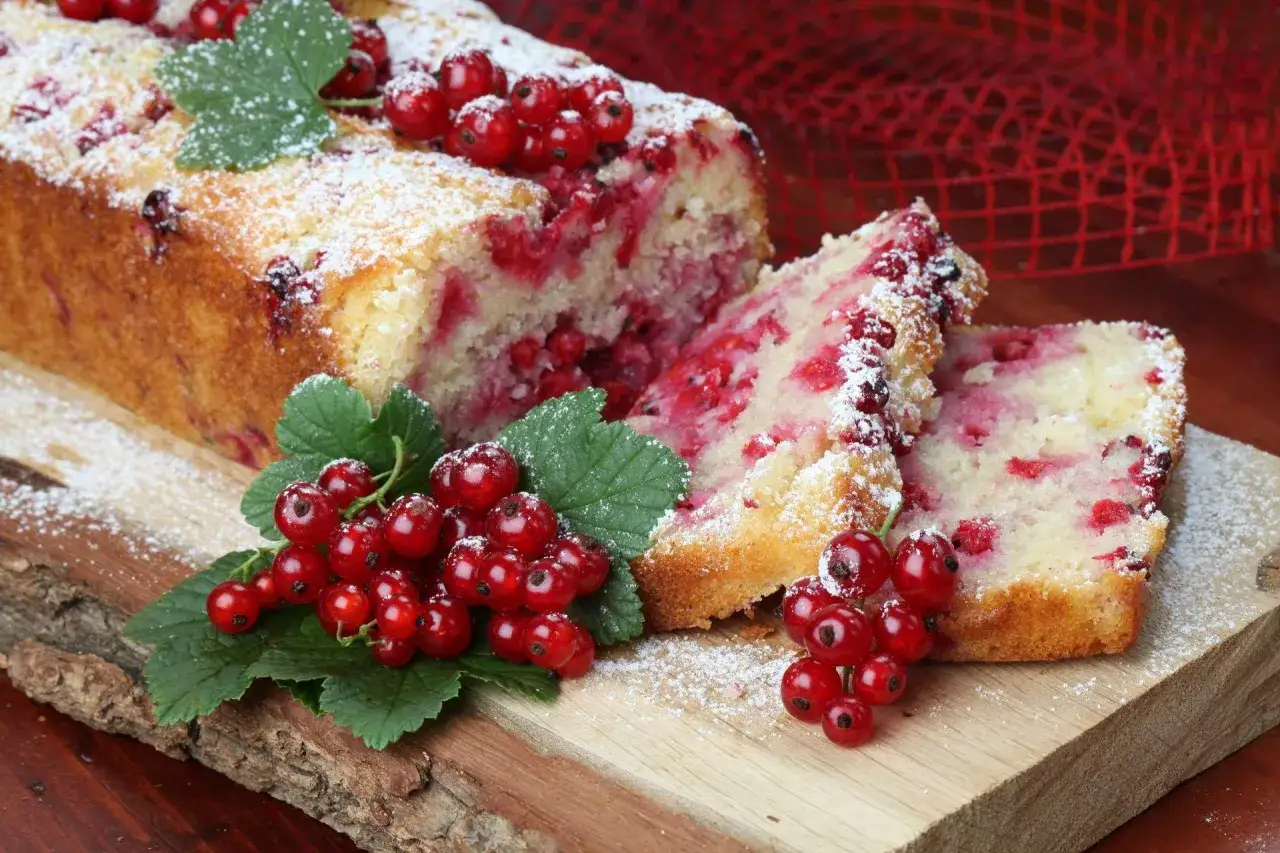 Szybkie ciasto z porzeczkami, posypane cukrem pudrem, z gałązkami świeżych owoców na drewnianej desce.