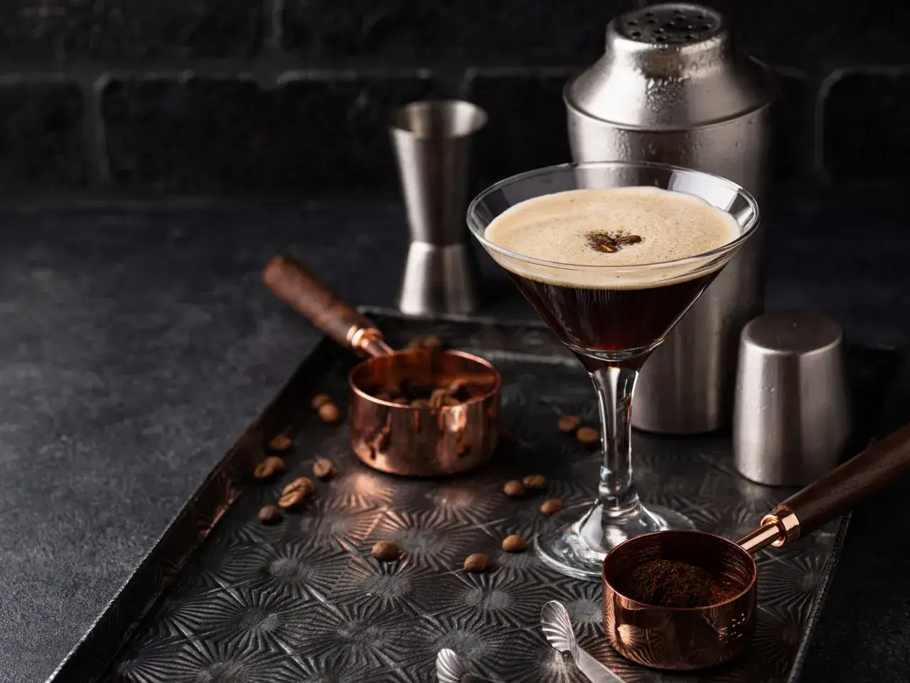Espresso martini przepis: kieliszek z kawowym drinkiem, shaker, ziarna kawy i miarki. Idealny na wieczór.